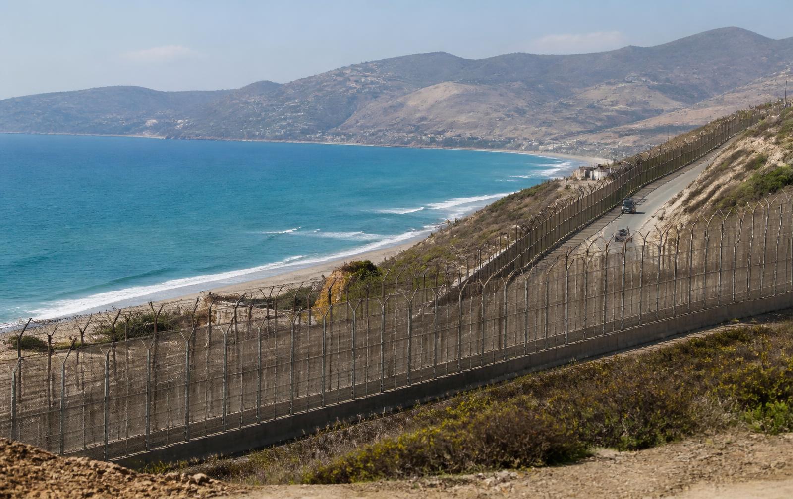 Grenzanlage der spanischen Exklave Ceuta an der Küste, dahinter das Meer und die Berge Marokkos