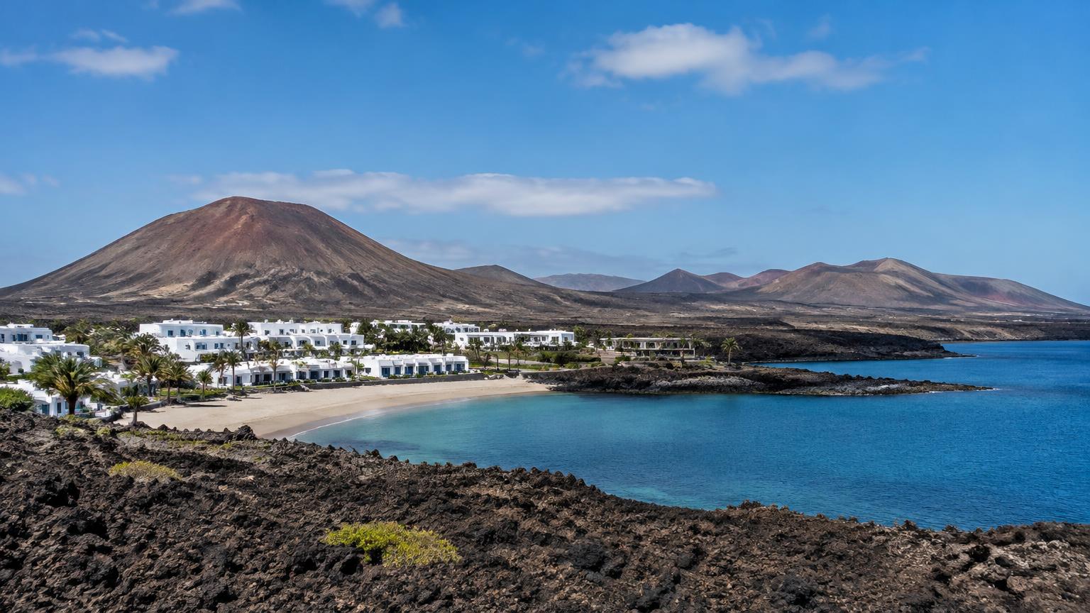 Weiße Ferienanlage an einer Bucht vor Vulkanbergen auf Lanzarote