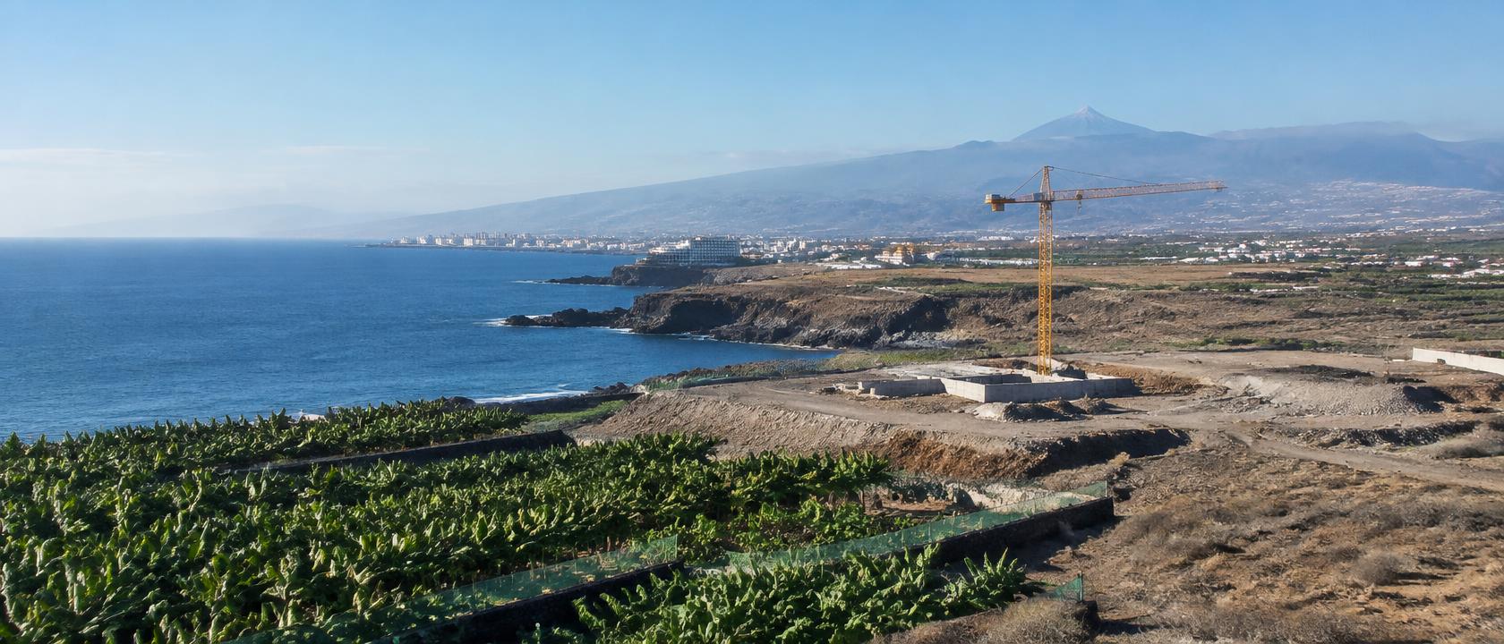 Küste im Süden Teneriffas mit Bananenplantagen und Baukran, im Hintergrund der Teide (KI-generierte Illustration)