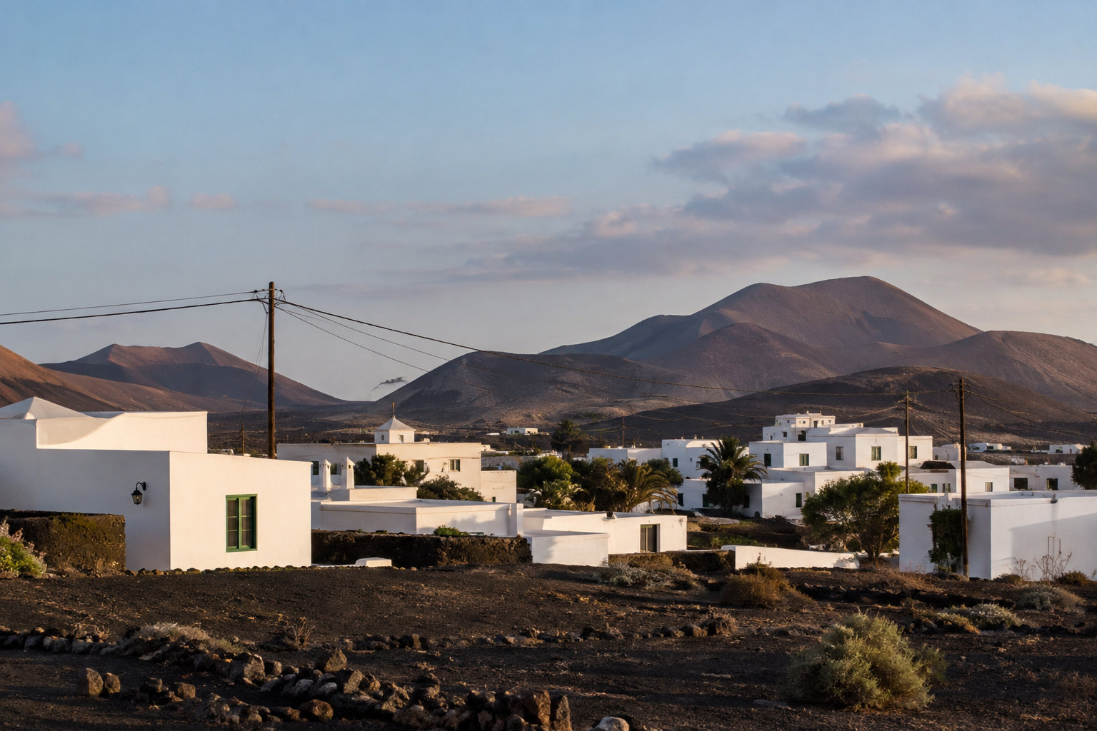 Weiße Häuser auf Lanzarote mit Strommasten vor vulkanischer Landschaft