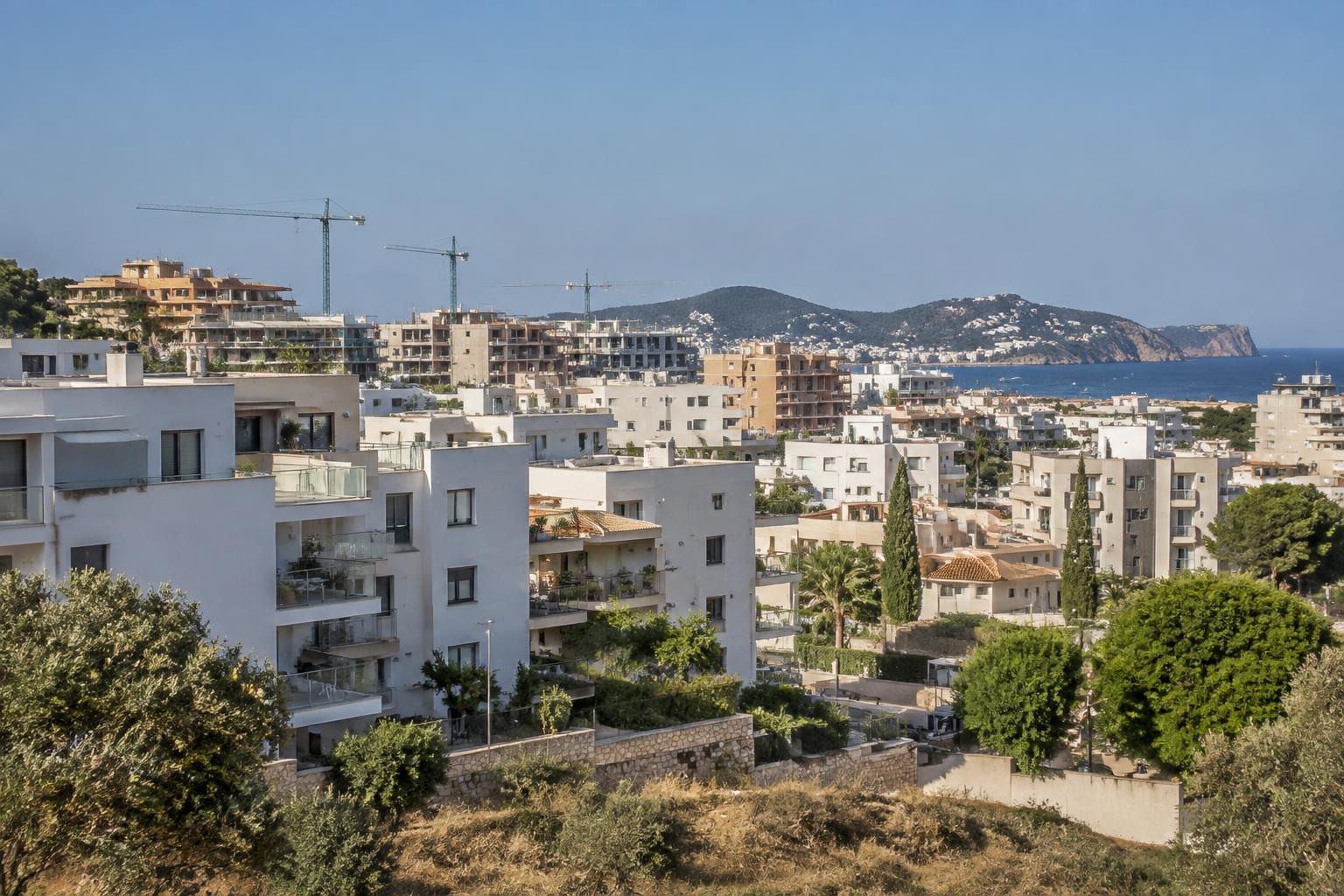 Wohnungsdefizit Ibiza: Wohngebäude und Baustellen am Rand einer Küstenstadt bei Tageslicht. Symbolbild – mit künstlicher Intelligenz erstellt